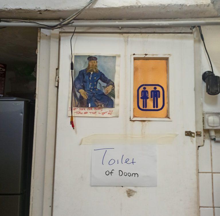 Picture of the bathroom door with a sign that says 'Toilet of doom' at the Postel